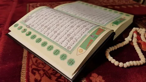 Open Quran book with white prayer beads on red prayer rug.